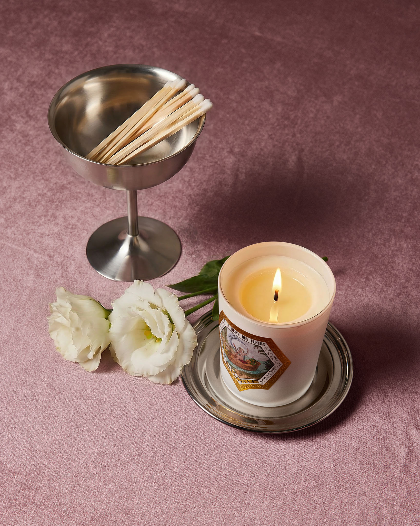Bougie parfumée À la Reine des Fleurs LT Piver allumée avec fleurs blanches et allumettes, ambiance florale élégante