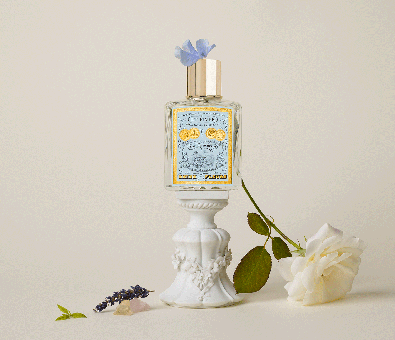 Ambiance raffinée avec flacon À la Reine des Fleurs entouré de fleurs délicates évoquant l’histoire et l’élégance royale.