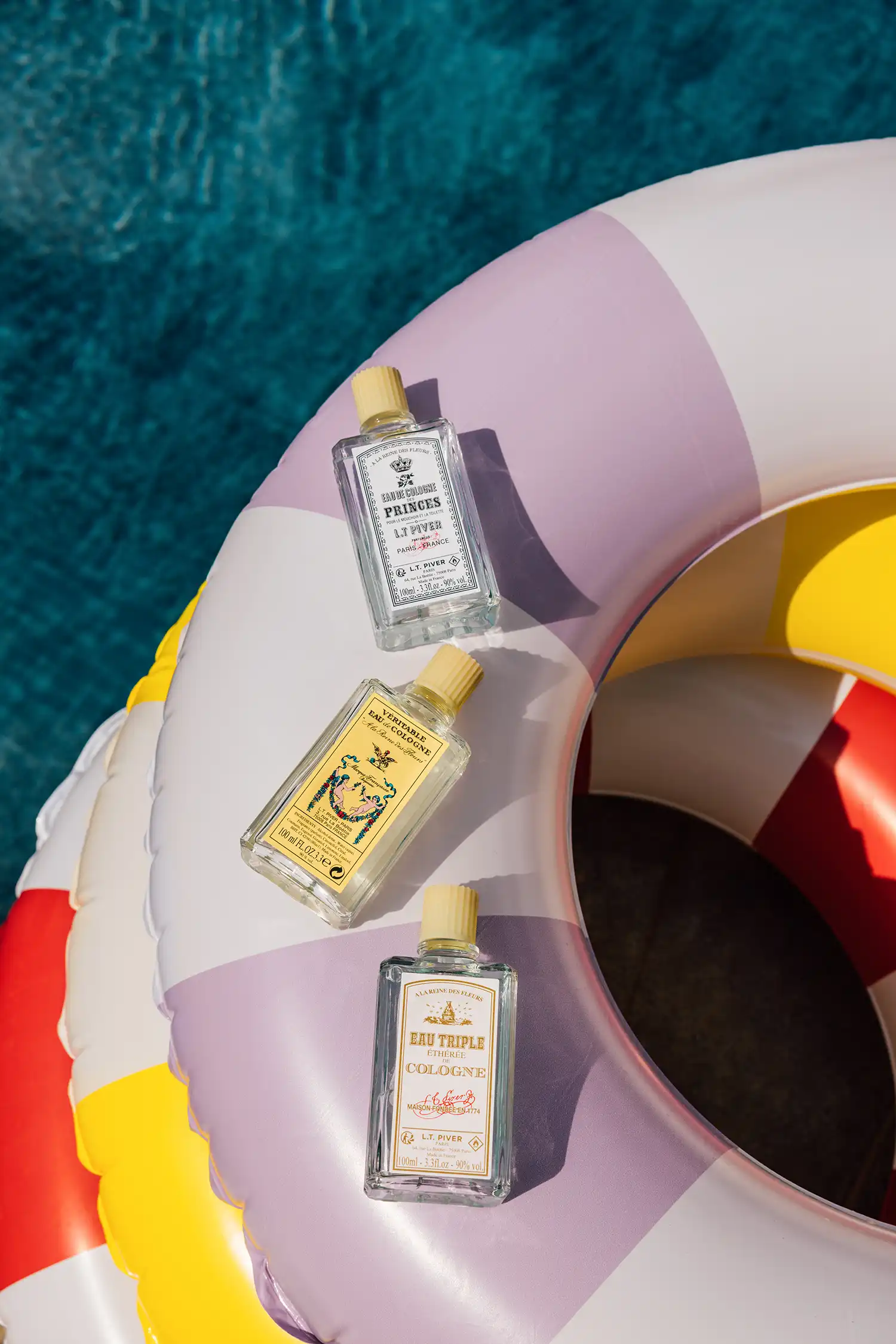 Flacons d’eaux de Cologne L.T. Piver posés sur une bouée colorée flottant sur l’eau, évoquant fraîcheur et légèreté estivale.